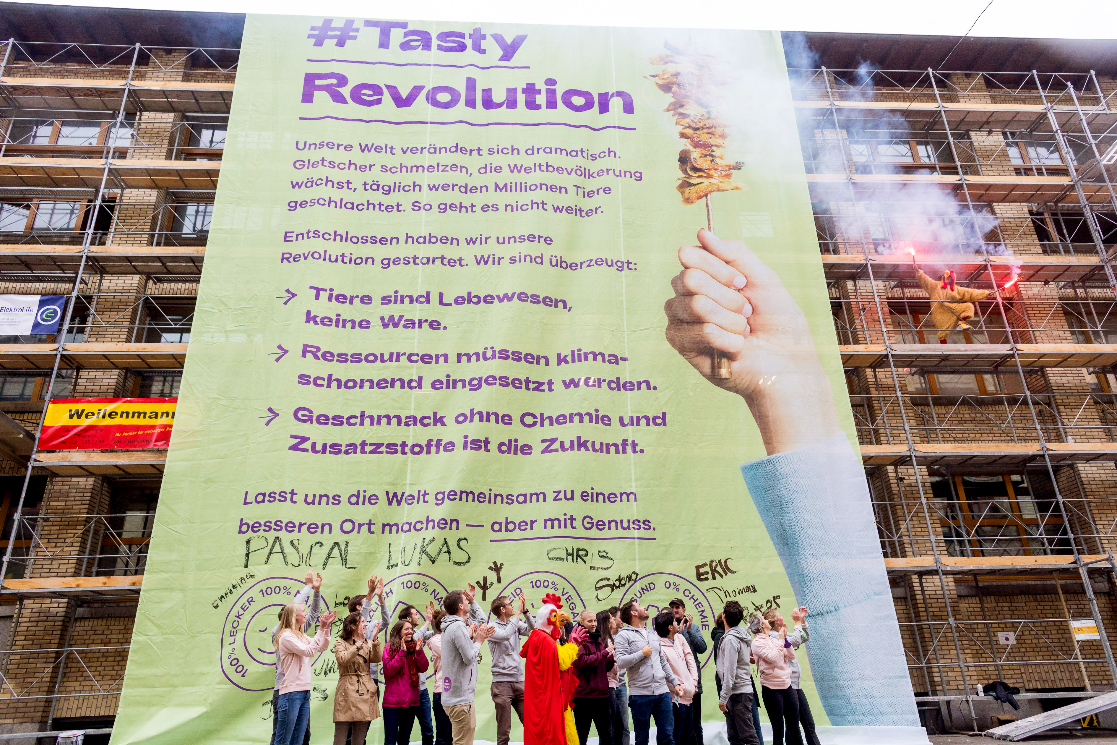 A giant '#Tasty Revolution' banner on a scaffolded building, with Planted employees cheering beneath it